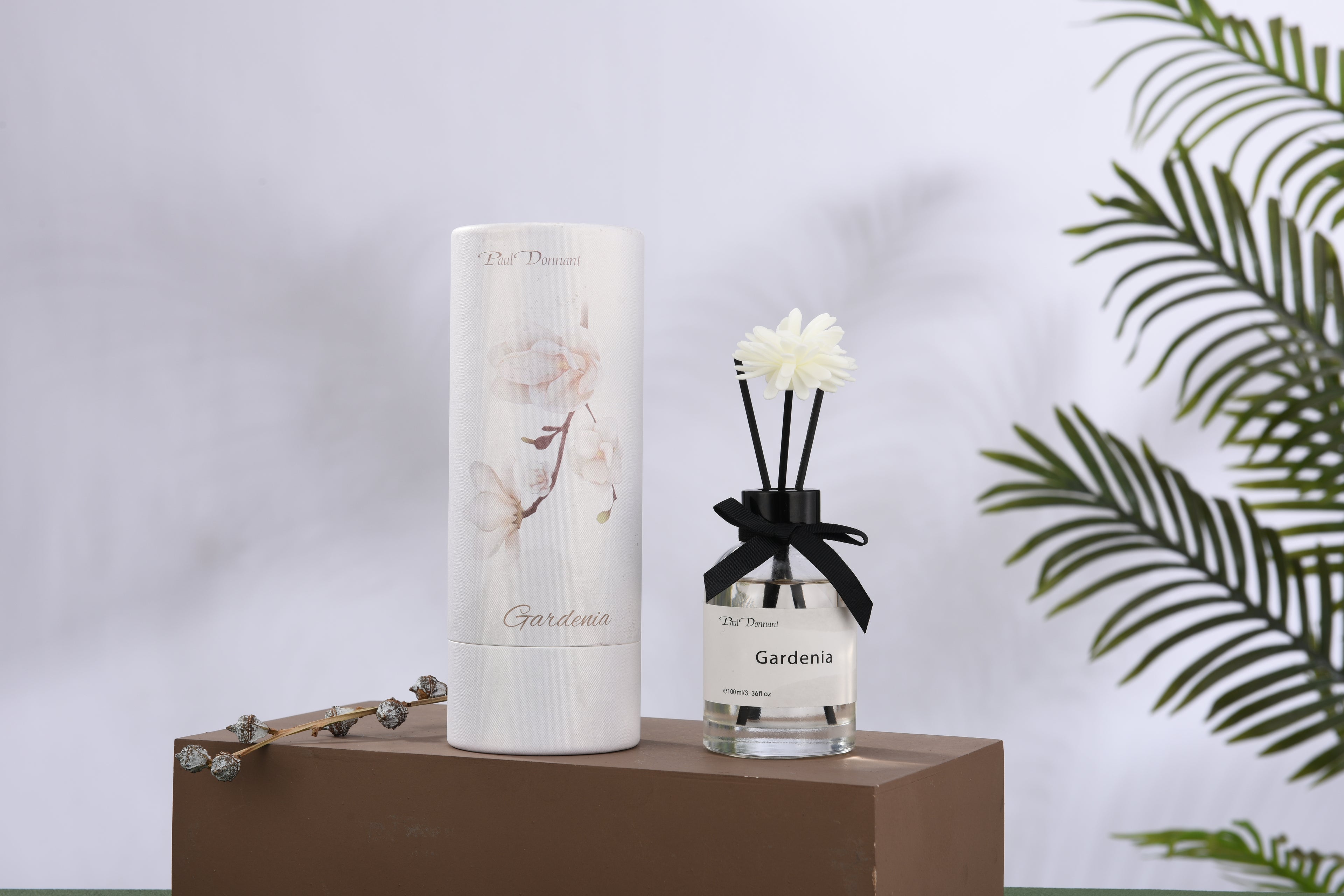 Gardenia-scented candle and diffuser on a wooden stand with a blurred plant background